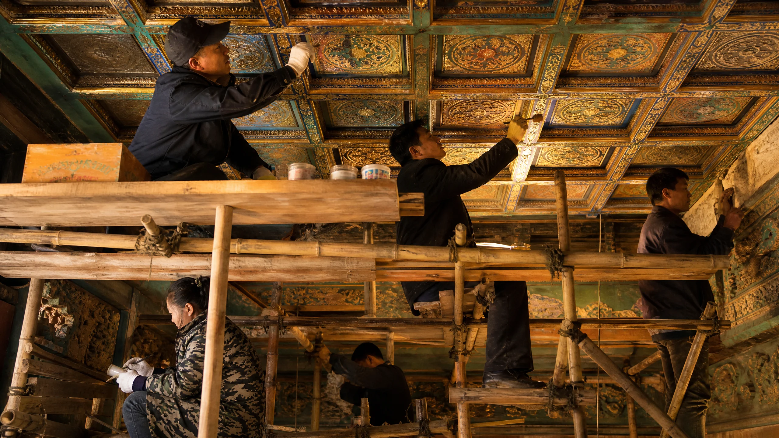 古建筑修复工程现场，‍工匠在脚手架上修复藻井彩画